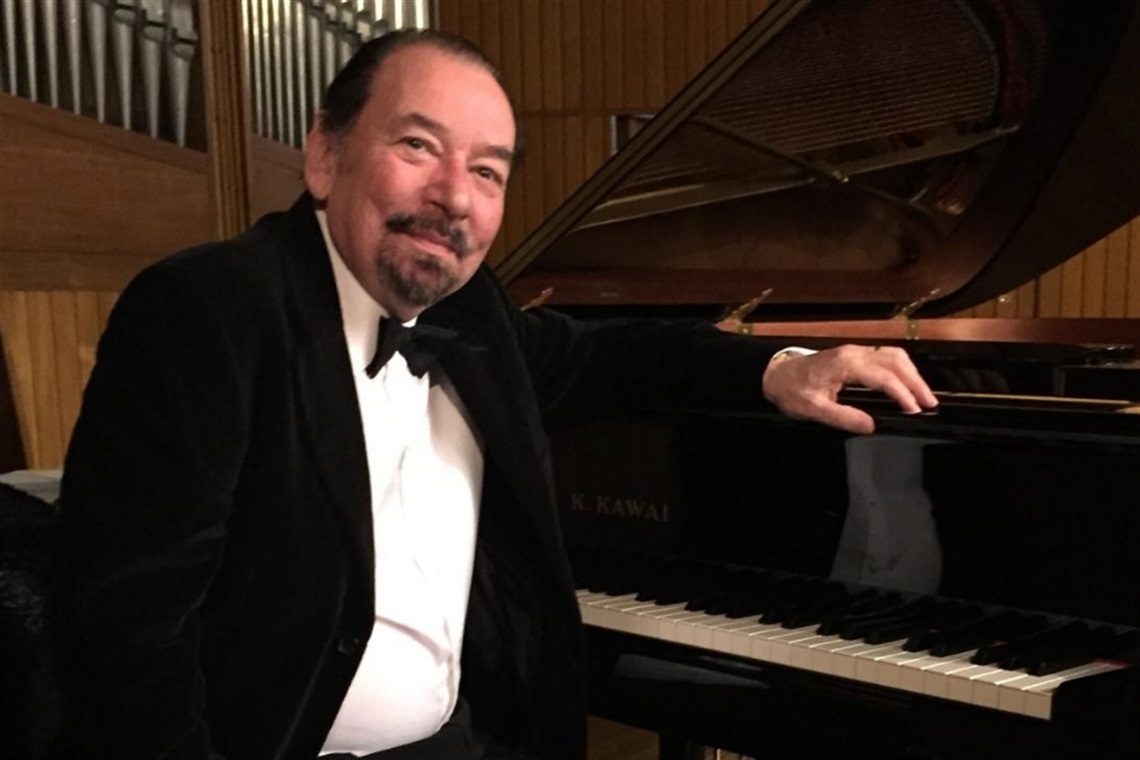 Image of David Scheel in a tux sitting side on next to a piano