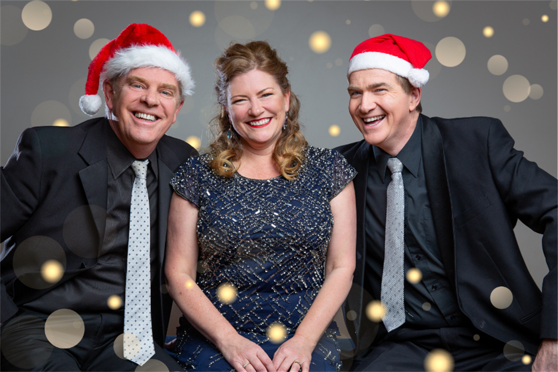 Two men and a woman smile at the camera, dressed in glamourous cocktail attire.