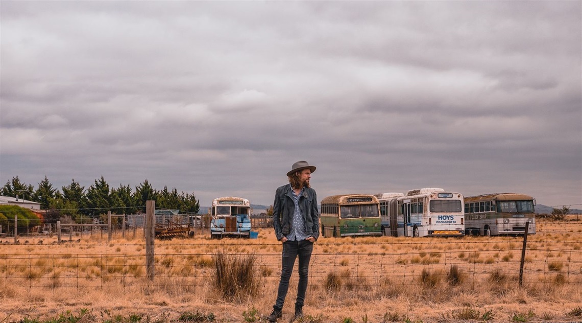 Shaun standing in a dry country landscape with old buses lined up in the background