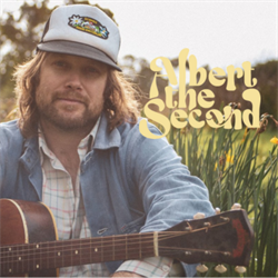 A man in a denim jacket and a trucker hat holding a guitar