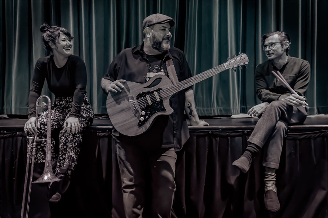 Lisa Baird, Lloyd Spiegel and Tim Burnham sitting on the edge of a stage talking together and laughing