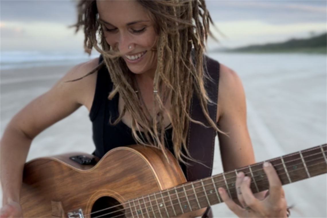 A young woman with dreadlocks playing guitar on the beach