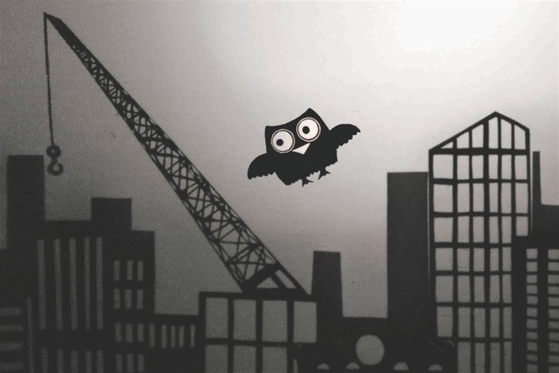 Black silhouette picture of an owl flying above buildings