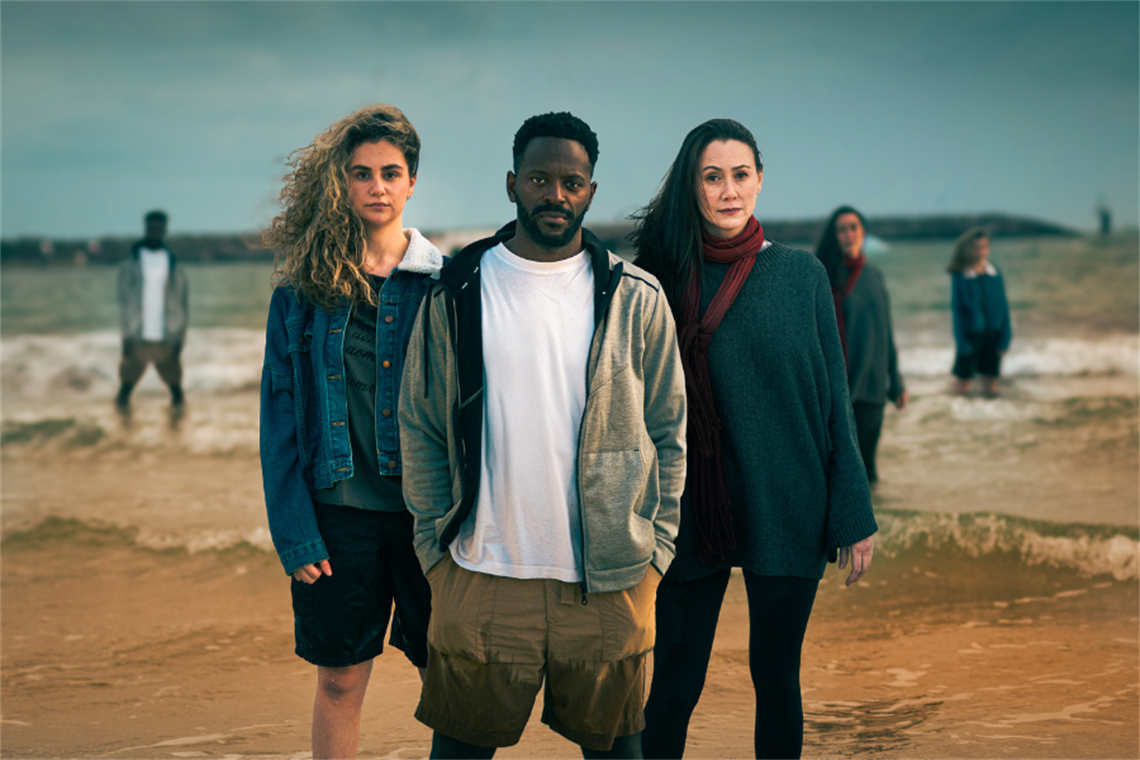 A man, a woman, and a girl standing ankle deep in the ocean, looking at the camera