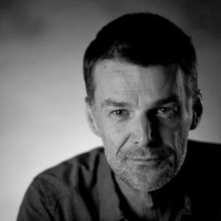 A close up black and white photo of Wayne Macauley, a middle aged man with short dark hair and grey stubble.