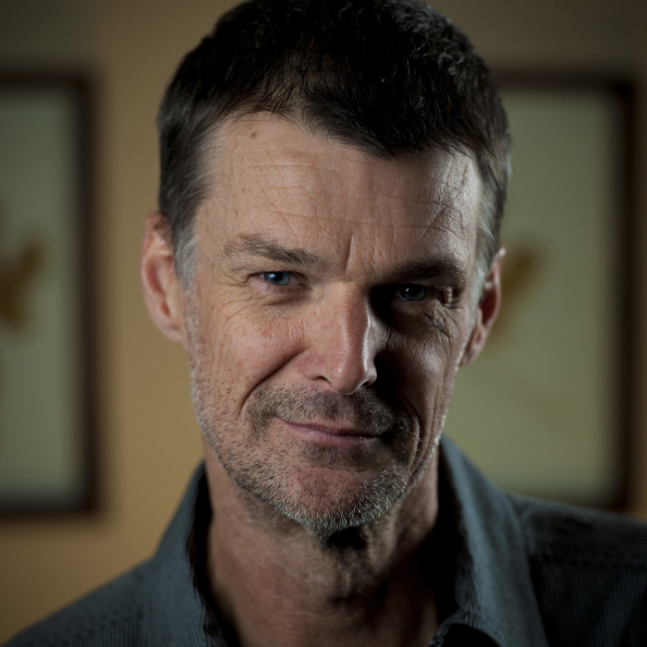 A close up black and white photo of Wayne Macauley, a middle aged man with short dark hair and grey stubble.